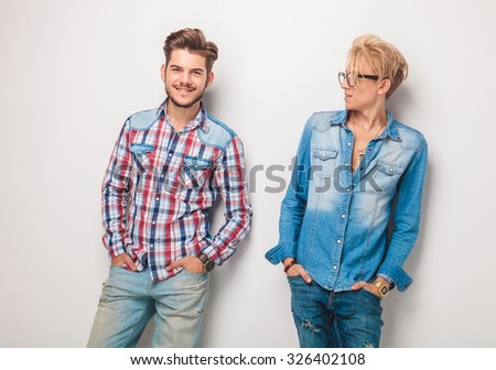 blond young casual man looking at his friend , standing against studio wall