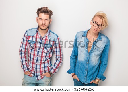 two young casual fashion men standing with hands in pockets against studio background