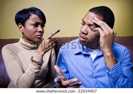A couple is fighting on a couch and the girl is pointing her finger accusingly at him.