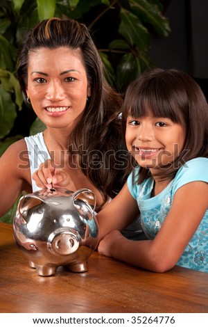 mom and daughter smile at the camera as they pose with a piggy bank