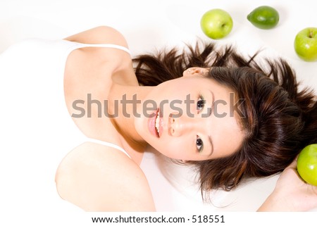 A pretty young asian woman lies on a white background with apples and limes