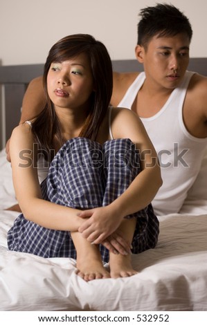 An asian couple sit on the bed not talking after an argument