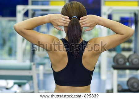 A female fitness instructor stretches with her hands behind her head