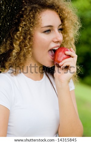 A pretty young woman outside in a park eating a red apple