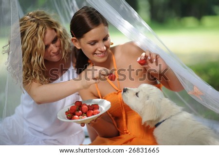 two young woman with puppy having picnic on meadow