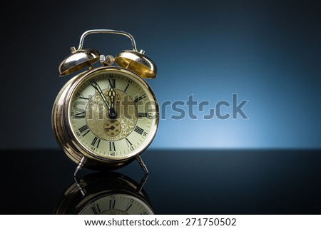 Vintage alarm clock showing five minutes to twelve, blue background, copy space