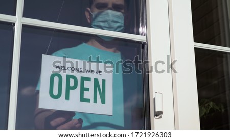 Close up of the male Caucasian hands turning a signboard on the glass door of the shop from CLOSED to OPEN. Reopening of a small business activity after quarantine covid-19 emergency.