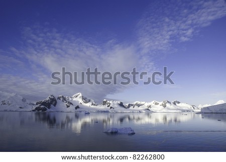 Deep blue sky, snow capped mountains and iceberg in foreground with calm waters. Taken at Paradise Harbor, Antarctica. With Copy Space (above).