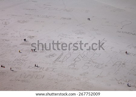 People walking over the flat land in front of Mont Saint-Michel, Normandy, France. Writings of visitors are visible in the sand.