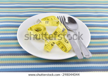 yellow measuring tape with spoon and fork on dish concept for healthy diet and body weight control.