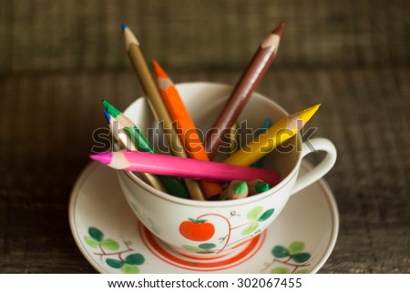 Colored pencils in a cup with flowers on an old table