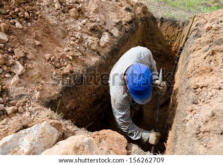 man in blue cap digs grave at cemetery
