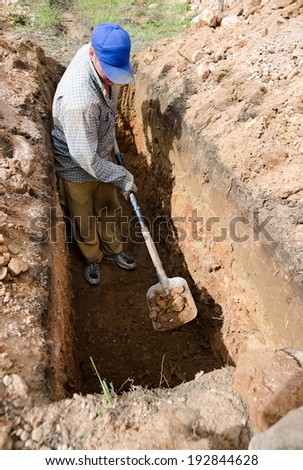 Caucasian man in blue cap digs grave at cemetery