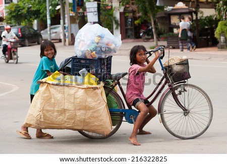 SIEM REAP, CAMBODIA - JUNE 28, 2014: Two local unidentified girls of school age pose for camera carrying large bags with trash on a bicycle. In Khmer family every member must earn money.