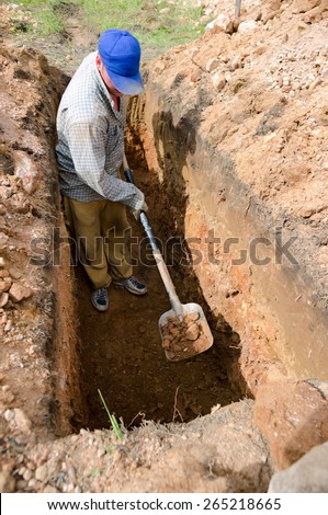 Caucasian man in blue cap digs grave at cemetery