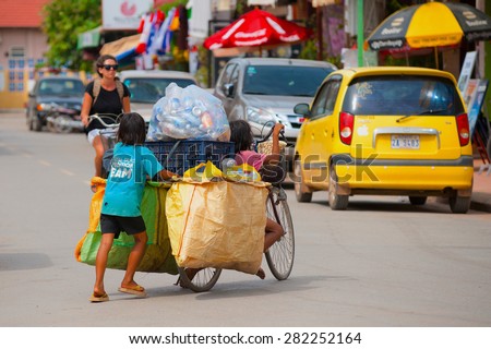 SIEM REAP, CAMBODIA - JUNE 28, 2014: Four local unidentified girls of school age carry large bags with different kinds of trash on a bicycle. In Khmer family every member must earn money.