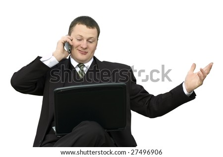 a young businessman with a slight smile in a dark suit with a laptop on his lap is talking on his cell phone