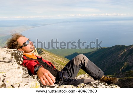 young man lies on stone having climbed up mountain top