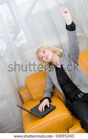 young joyful blonde woman sits on sofa with laptop, arm raised up