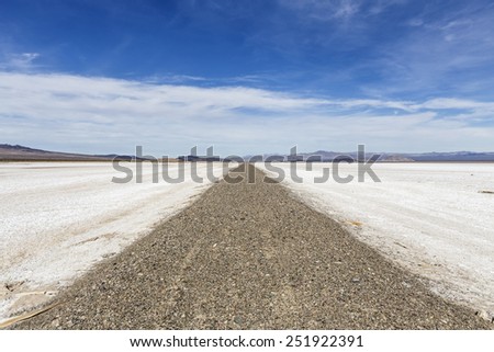 Old closed road crossing vast salt flat dry lake in California\'s Mojave National Preserve.