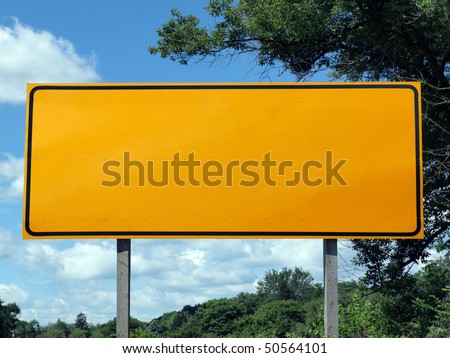Big blank highway sign with blue sky and summer greens.