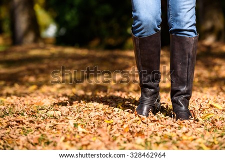 Woman walking through fall leaves, legs and feet only