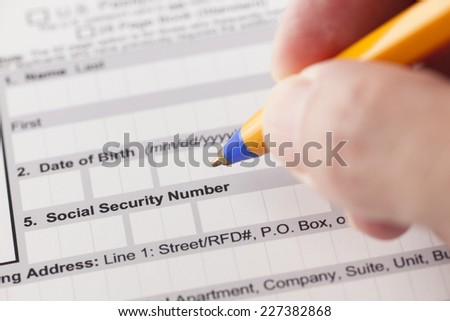 Social security number fields in application form and human hand with ballpoint pen.