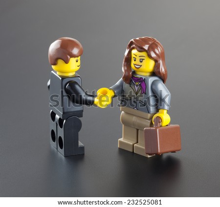 Tambov, Russian Federation - October 04, 2013 Lego minifigures businessman and businesswoman with suitcase shaking hands on black background. Studio shot.