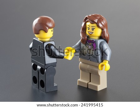 Tambov, Russian Federation - October 04, 2013 Lego minifigures businessman and businesswoman shaking hands on black background.