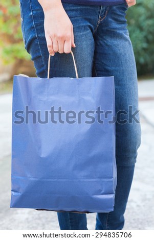 Woman standing on the street with blue paper bag in her hand.