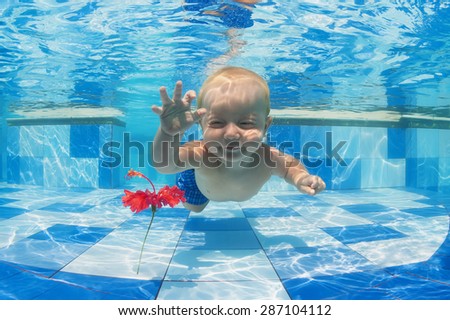 Smiling baby boy diving underwater with fun for red flower in blue pool Active lifestyle, child swimming lesson with parents, and water sports activity during family summer vacation in tropical resort