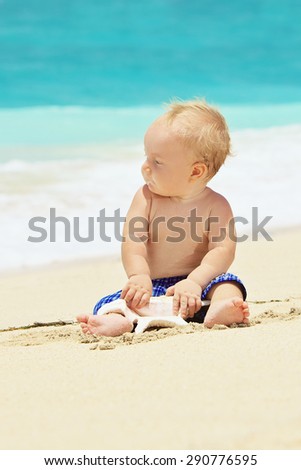 Portrait of child sitting and playing alone with sea shell with fun on balinese sand ocean beach before swimming. Family lifestyle, water leisure on summer vacation with baby on tropical Bali island