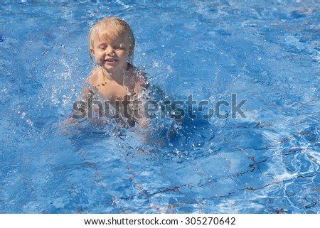 Happy smiling baby has fun jumping with splashes in blue water in pool before swimming lessons. Healthy lifestyle, active parents, and people water sports activity on summer family vacation with baby.