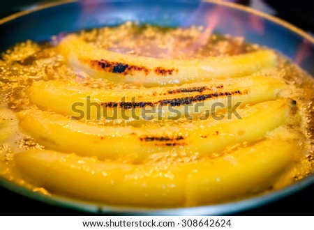 Bananas flambe with orange flame of burning rum, cooking process. Selective focus on the central banana.