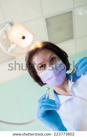 Portrait of woman dentist wearing surgical mask while holding angled mirror and drill selective focus