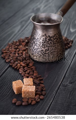 Three pieces of brown sugar surrounded by coffee beans with hot coffee pot on back. Rustic wooden background.