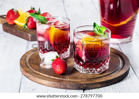 Sangria with fresh oranges, strawberries, mint and ice on white wooden background. Selective focus.