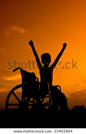 Boy sitting in wheel chair at sunset signaling victory