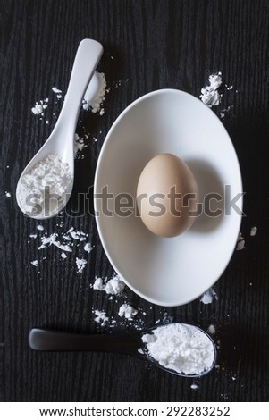 Eggs in a bowl, spoon the flour on a wooden table in black.