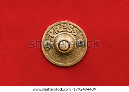 Classic traditional rustic heavy cast brass doorbell button on a seamless red wall shot straight on.
