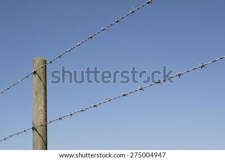 Wooden barbed wire fence post on a sunny blue sky.