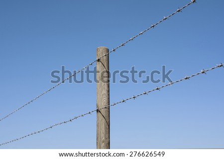 Barbed wire fence post against a clear blue sky.
