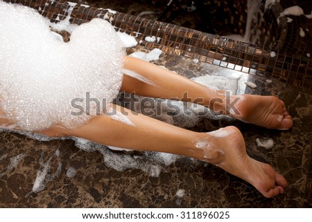 Soap massage in the hammam, the legs of a young woman covered with foam.