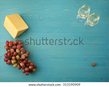 two glasses of white wine, a piece of cheese and a bunch of grapes on a blue wooden background