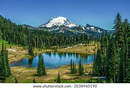 Lake on the background of a snowy mountain peak. Mountain forest lake landscape. Lake in mountain forest