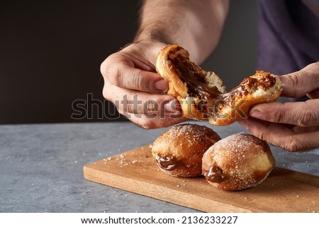 man's hand breaking a Berliner stuffed with dulce de leche. The berliners are also known as berlin balls, bollo, bolinha or bolas de fraile Foto stock © 