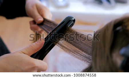 Professional hairdresser, stylist doing hairstyle and using straightener on beautiful long hair of client in white make up room. Beauty and haircare concept ストックフォト © 