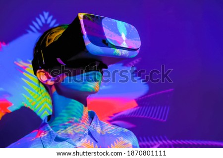 Woman using virtual reality headset, looking around at interactive technology exhibition with multicolor projector light illumination. VR, augmented reality, immersive, entertainment concept