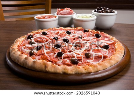 Calabrian sausage pizza, typical Brazilian pizza, on wooden board over table background, pizza ingredients make up the backdrop.
