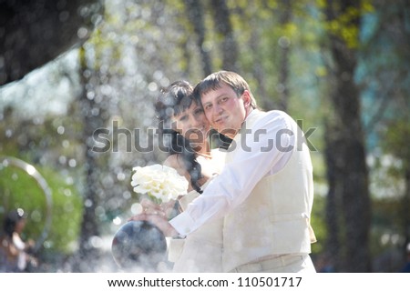 Happy bride and groom with bouquet near fountain